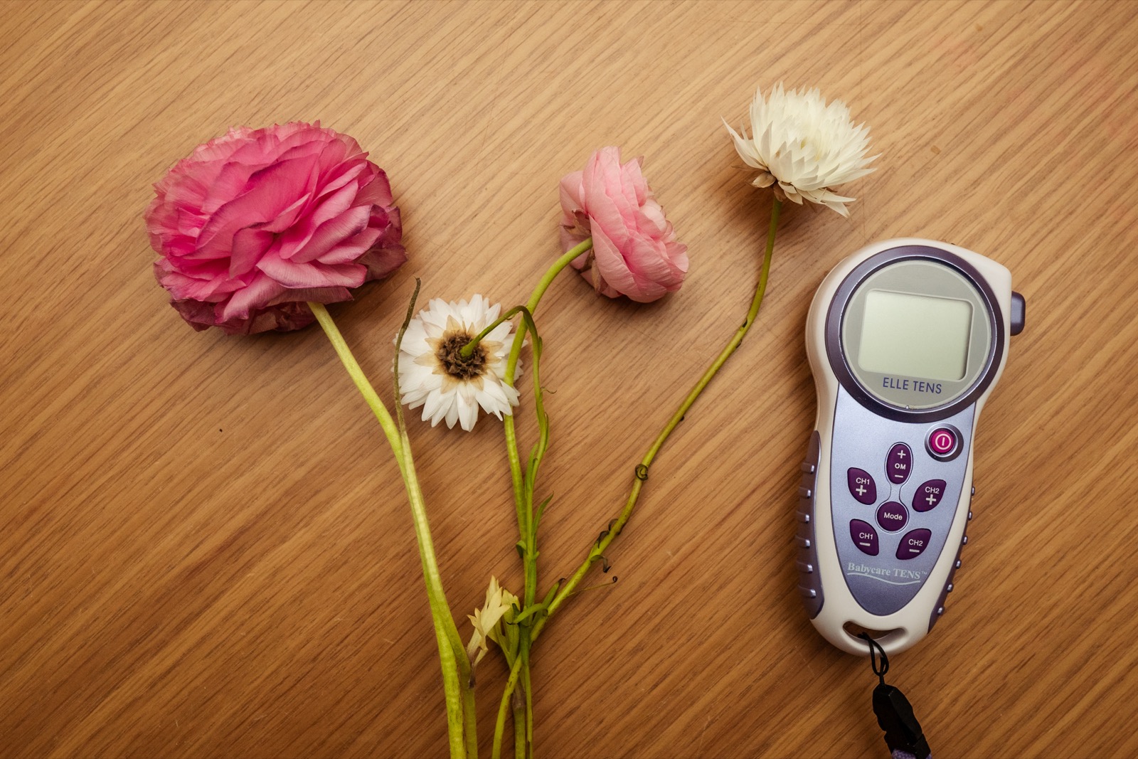 ELLETENS 2 TENS machine resting beside soft flowers on a wooden surface